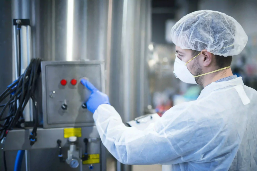 A man wearing a white coat and hat is focused on working with a machine in a laboratory environment.