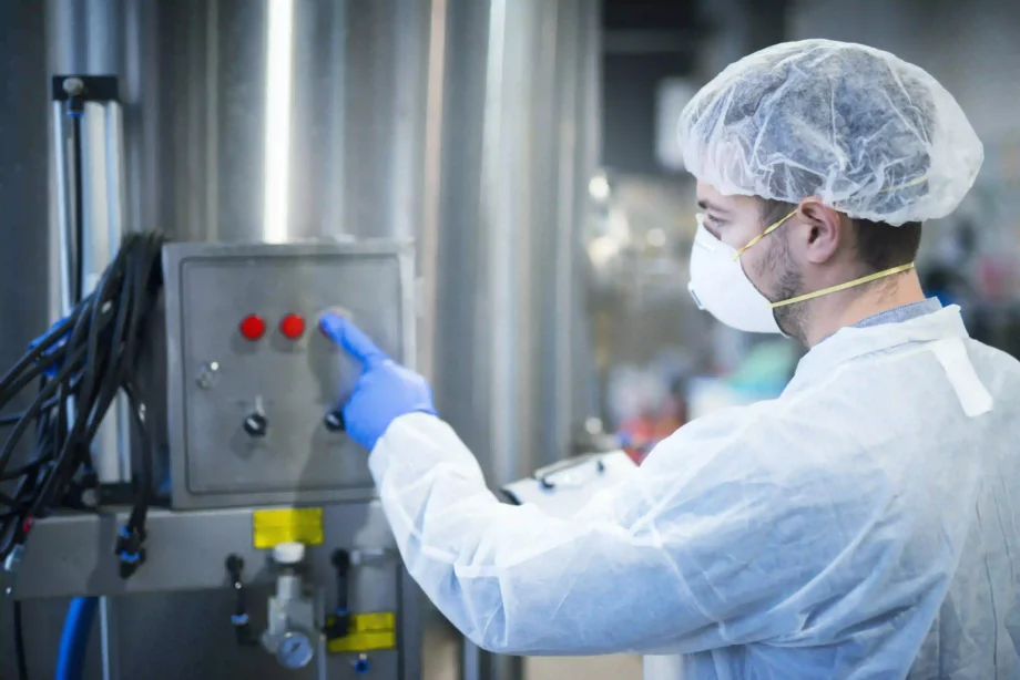 A man wearing a white coat and hat is focused on working with a machine in a laboratory environment.