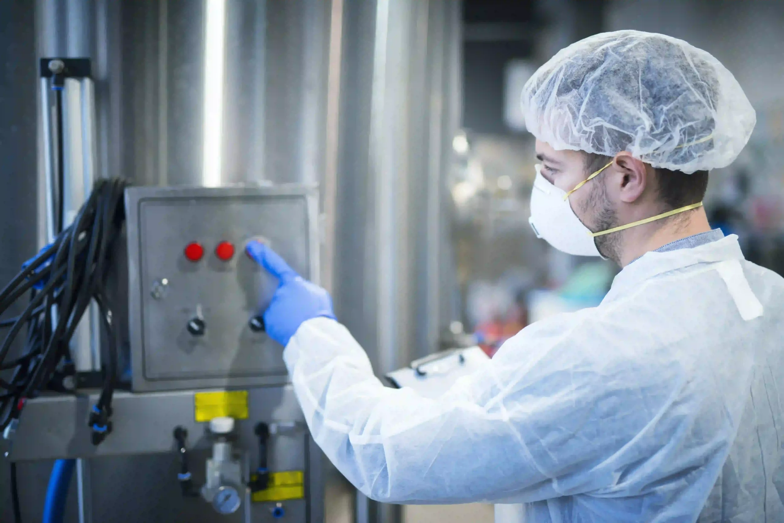 A man wearing a white coat and hat is focused on working with a machine in a laboratory environment.